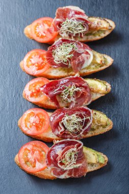 Meze bruschetta salam, domates, kabak ciabatta ekmeği taş arduvaz arka plan üzerinde tarih ile kapatın. Lezzetli aperatifler, sandviçler, crostini, parti ya da piknik zamanında antipasti. Üstten Görünüm