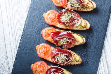 Meze bruschetta salam, domates, kabak ciabatta ekmeği taş arduvaz arka plan üzerinde tarih ile kapatın. Lezzetli aperatifler, sandviçler, crostini, parti ya da piknik zamanında antipasti. Üstten Görünüm