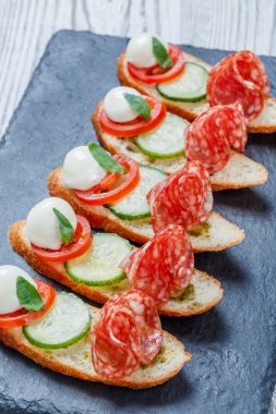 Caprese sandviç domates, mozzarella peyniri, fesleğen, salam taş arduvaz arka plan üzerinde ciabatta ekmeği üzerine kapatın. Lezzetli meze aperatifler, bruschetta, crostini, antipasti. Üstten Görünüm