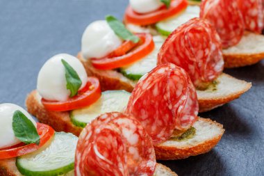 Caprese sandviç domates, mozzarella peyniri, fesleğen, salam taş arduvaz arka plan üzerinde ciabatta ekmeği üzerine kapatın. Lezzetli meze aperatifler, bruschetta, crostini, antipasti. Üstten Görünüm