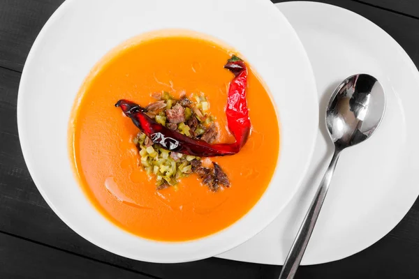 Томатний суп, суп з червоного перцю, соус з оливковою олією, м'ясо та соління в мисці на чорному дерев'яному фоні, здорова їжа. Вид зверху — стокове фото