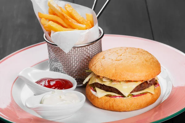 Cheeseburger, hamburger con patatine fritte, ketchup, maionese, verdure fresche e formaggio su piatto su fondo di legno scuro. Fast food americano — Foto Stock