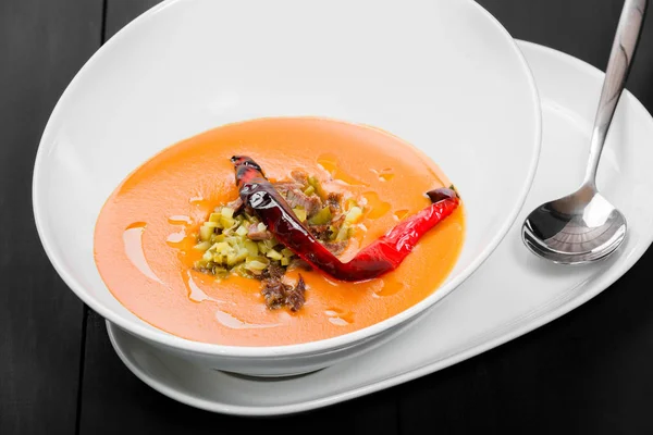 Томатний суп, суп з червоного перцю, соус з оливковою олією, м'ясо та соління в мисці на чорному дерев'яному фоні, здорова їжа. Вид зверху — стокове фото