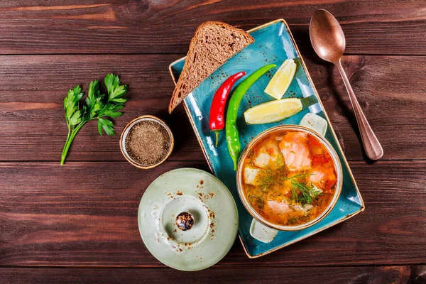 Рыбный суп с лососем и креветками, укроп, картофель, лимон, перец и хлеб на темном деревянном фоне, здоровая пища. Вид сверху — стоковое фото