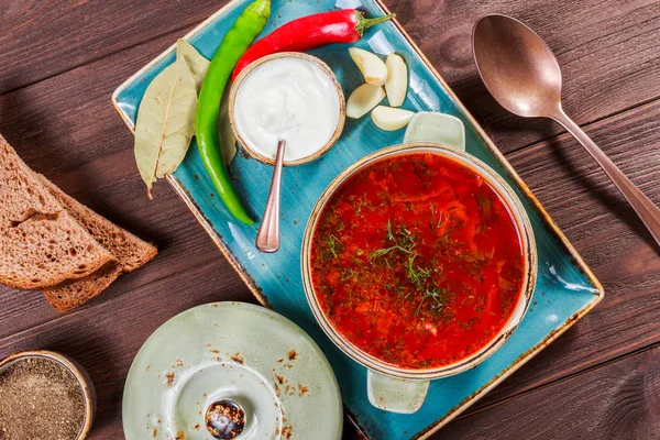 Sopa de remolacha tradicional ucraniana y rusa: borscht en maceta de barro con crema agria, especias, ajo, pimienta, hierbas secas y pan sobre fondo de madera oscura, comida saludable. Ingredientes en la mesa . — Foto de Stock