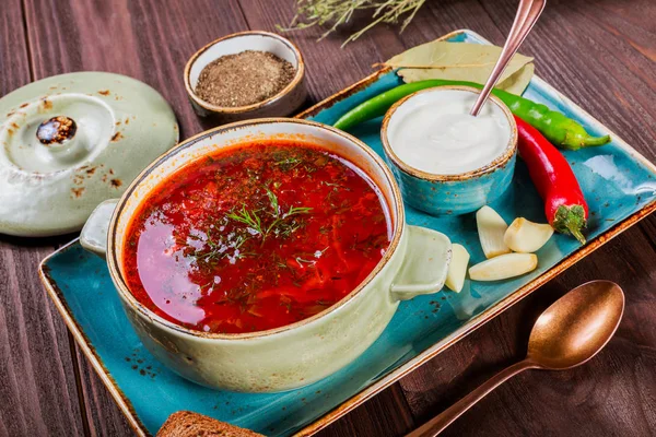 Sopa de remolacha tradicional ucraniana y rusa: borscht en maceta de barro con crema agria, especias, ajo, pimienta, hierbas secas y pan sobre fondo de madera oscura, comida saludable. Ingredientes en la mesa . — Foto de Stock