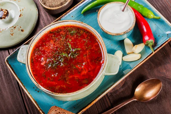 Sopa de remolacha tradicional ucraniana y rusa: borscht en maceta de barro con crema agria, especias, ajo, pimienta, hierbas secas y pan sobre fondo de madera oscura, comida saludable. Ingredientes en la mesa . — Foto de Stock