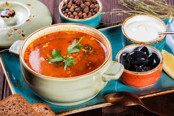 Soppa med kött, oliver, örter, citron, gräddfil i skål, svart bröd och kryddor på mörk trä bakgrund, hemlagad mat. Traditionell rysk soppa - solyanka. Ovanifrån — Stockfoto