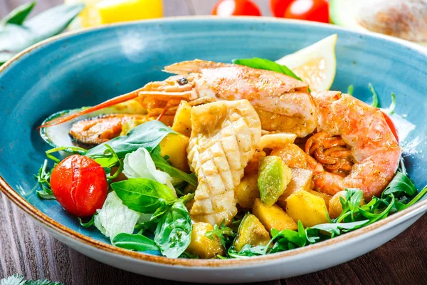 Warm salad with seafood, langoustine, mussels, shrimps, squid, scallops, mango, pineapple, avocado, arugula and basil on wooden background close up. Mediterranean food. Top view — Stock Photo, Image