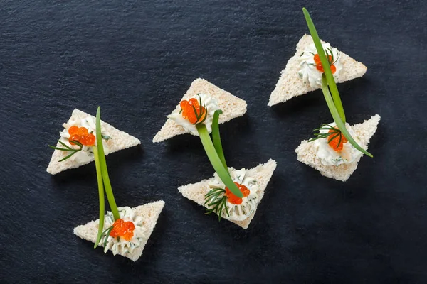 Appetizer canape with red caviar and cream cheese on stone slate background close up. Delicious snacks, sandwiches, crostini, brushetta, antipasti on party or picnic time. Top view