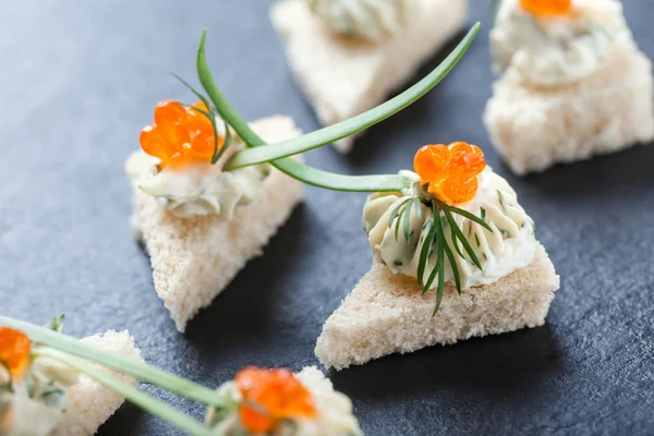 Appetizer canape with red caviar and cream cheese on stone slate background close up. Delicious snacks, sandwiches, crostini, brushetta, antipasti on party or picnic time. Top view
