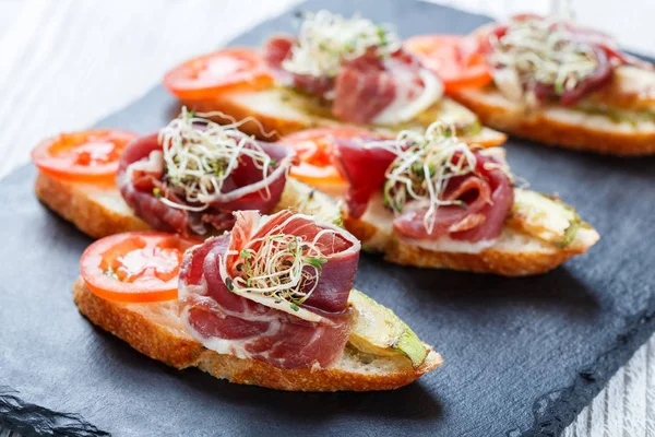 Meze bruschetta salam, domates, kabak ciabatta ekmeği taş arduvaz arka plan üzerinde tarih ile kapatın. Lezzetli aperatifler, sandviçler, crostini, parti ya da piknik zamanında antipasti. Üstten Görünüm