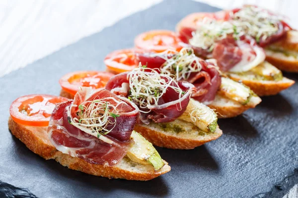 Meze bruschetta salam, domates, kabak ciabatta ekmeği taş arduvaz arka plan üzerinde tarih ile kapatın. Lezzetli aperatifler, sandviçler, crostini, parti ya da piknik zamanında antipasti. Üstten Görünüm