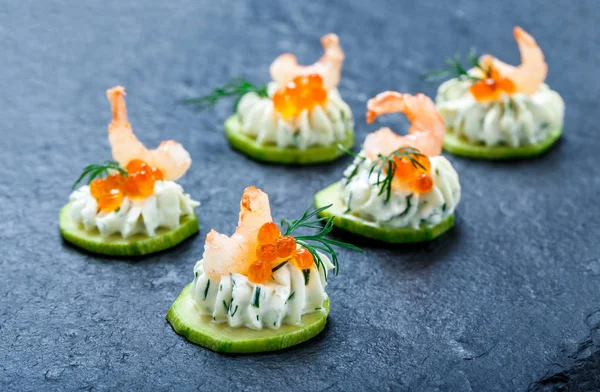 Appetizer canape with red caviar, shrimp and cream cheese on stone slate background close up. Delicious snacks, sandwiches, crostini, bruschetta, antipasti on party or picnic time. Top view