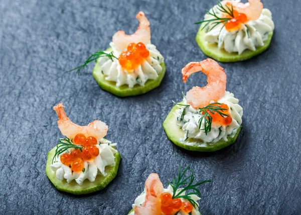 Appetizer canape with red caviar, shrimp and cream cheese on stone slate background close up. Delicious snacks, sandwiches, crostini, bruschetta, antipasti on party or picnic time. Top view