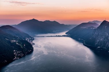 Dağlar ve akşam şehir Lugano dramatik günbatımı sırasında İsviçre Alpleri üzerinde çevrili lake Lugano hava görünümünü. Seyahat