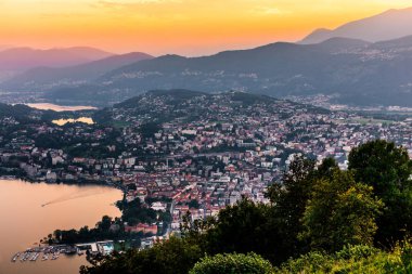 Dağlar ve akşam şehir Lugano dramatik günbatımı sırasında İsviçre Alpleri üzerinde çevrili lake Lugano hava görünümünü. Seyahat