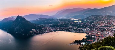 Dağlar ve akşam şehir Lugano dramatik günbatımı sırasında İsviçre Alpleri üzerinde çevrili lake Lugano hava görünümünü. Seyahat