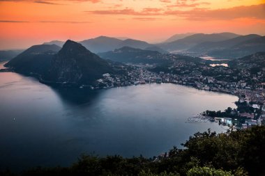 Dağlar ve akşam şehir Lugano dramatik günbatımı sırasında İsviçre Alpleri üzerinde çevrili lake Lugano hava görünümünü. Seyahat