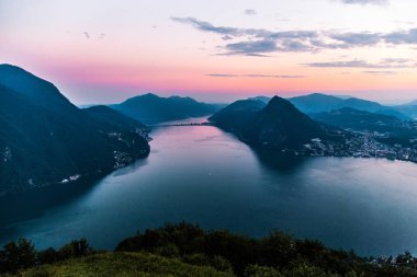 Dağlar ve akşam şehir Lugano dramatik günbatımı sırasında İsviçre Alpleri üzerinde çevrili lake Lugano hava görünümünü. Seyahat