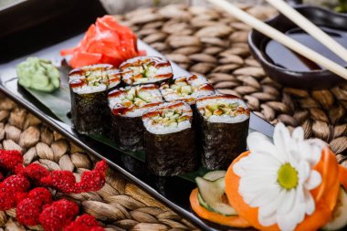 Suşi Roll - Maki Sushi füme yılan balığı, salatalık ve avokado çiçeklerle süslenmiş bambu mat siyah taş. Japon mutfağı