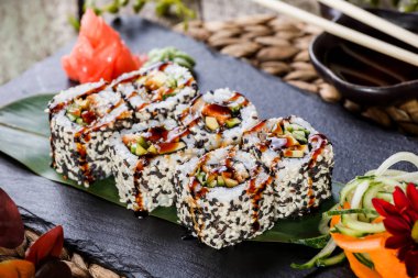 Suşi kara taş üzerine bambu hasır, seçici odak üzerinde set karides tempura, salatalık, avokado ve susam ile alır. Japon mutfağı