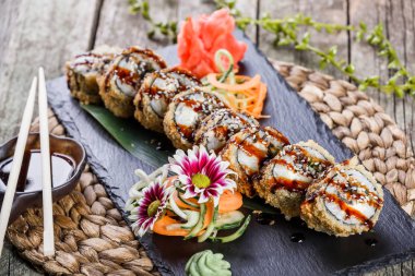 Sıcak kızarmış suşi rulo ve maki ile füme yılan balığı, krem peynir, avokado ve wasabi kara taş üzerine bambu hasır, seçici odak üzerinde ayarlayın. Japon mutfağı