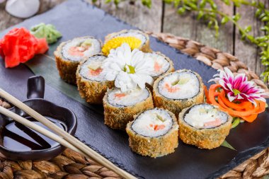 Sıcak kızarmış suşi Roll - Maki Sushi somon, salatalık, avokado ve krem peynir çiçeklerle süslenmiş bambu mat siyah taş. Japon mutfağı