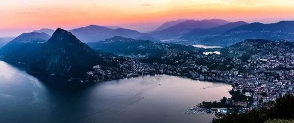 Vista aérea del lago Lugano rodeado de montañas y ciudad nocturna Lugano durante la dramática puesta de sol, Suiza, Alpes. Viajes — Foto de Stock