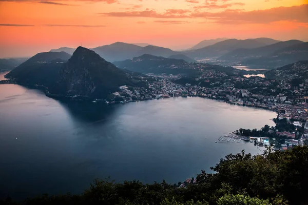 Vista aérea del lago Lugano rodeado de montañas y ciudad nocturna Lugano durante la dramática puesta de sol, Suiza, Alpes. Viajes — Foto de Stock