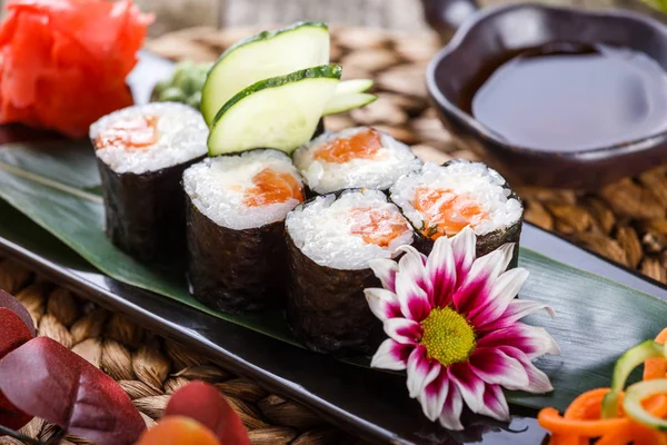 Sushi Roll - Sushi Maki hecho de salmón, queso crema, aguacate y wasabi sobre piedra negra sobre estera de bambú decorada con flores. Cocina japonesa — Foto de Stock