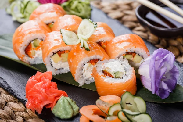 Rollos de sushi engastados con salmón, queso crema, caviar rojo, aguacate y wasabi sobre piedra negra sobre estera de bambú, enfoque selectivo. Cocina japonesa — Foto de Stock
