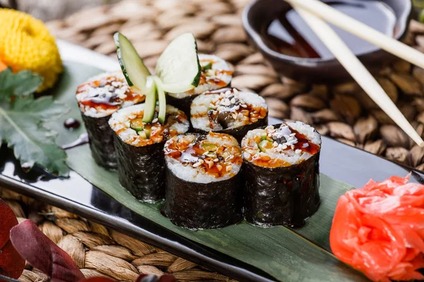 Sushi Roll - Sushi Maki con anguila ahumada, pepino, aguacate y sésamo sobre piedra negra sobre estera de bambú decorada con flores. Cocina japonesa — Foto de Stock