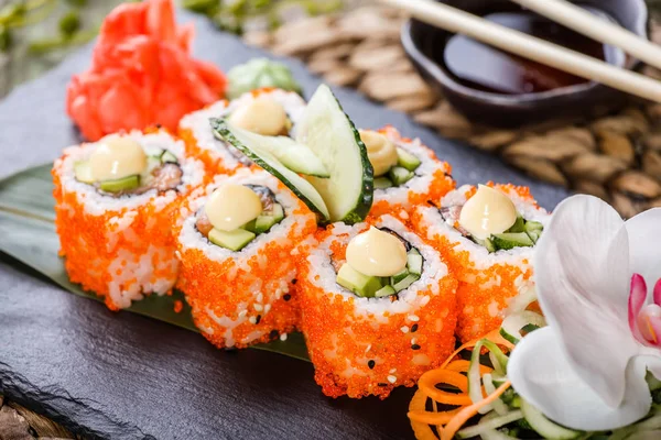 Sushi Roll - Sushi Maki hecho de salmón, caviar rojo, pepino, aguacate y queso crema sobre piedra negra sobre estera de bambú decorada con flores. Cocina japonesa — Foto de Stock