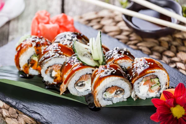 Rollos de sushi engastados con salmón, queso crema, pepino, sésamo y wasabi sobre piedra negra sobre estera de bambú, enfoque selectivo. Cocina japonesa — Foto de Stock