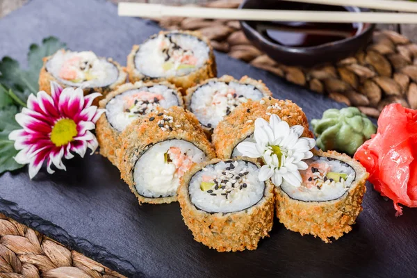 Rollos de sushi fritos y maki con carne de cangrejo, queso crema, aguacate y wasabi en piedra negra en estera de bambú, enfoque selectivo. Cocina japonesa — Foto de Stock