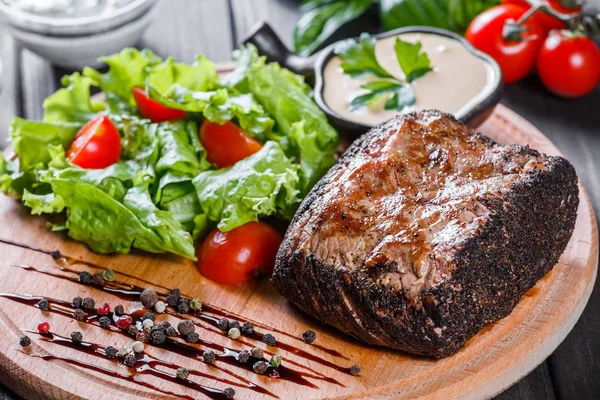 Vepřový grilovaný steak s zeleninový salát, rajčaty a omáčkou na dřevěném prkénku — Stock fotografie