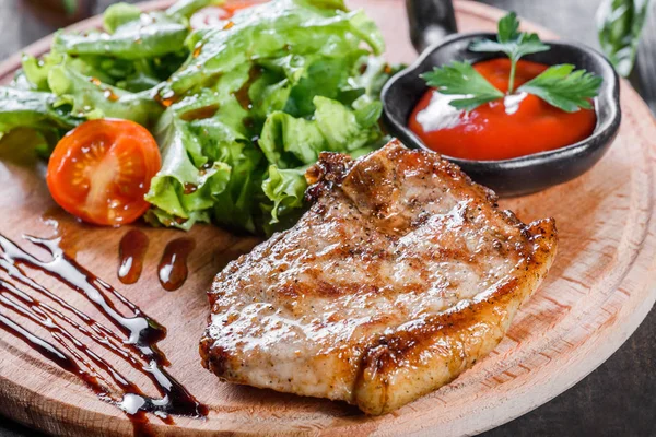 Grilled steak pork with fresh vegetable salad, tomatoes and sauce on wooden cutting board — Stock Photo, Image