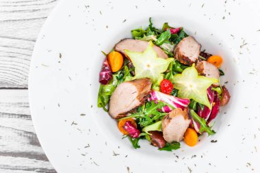 Taze salata tavuk göğsü, roka, marul, karnabahar, physalis ve ahşap arka plan üzerinde plaka üzerinde carambola ile kapatın. Üstten Görünüm