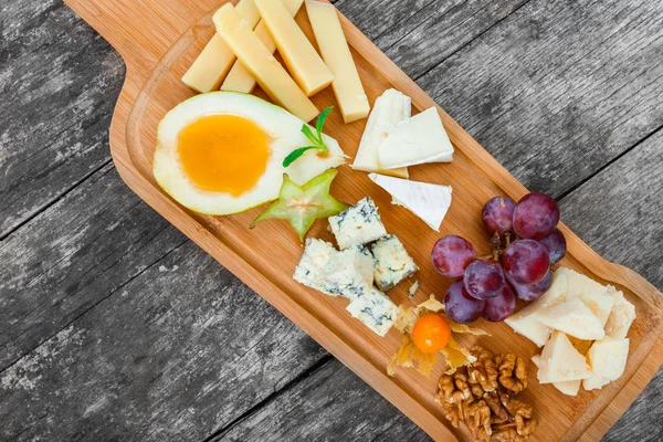 Cheese platter garnished with pear, honey, walnuts, grapes, carambola, physalis on cutting board on wooden background. Snacks and Wine appetizers set. Top view — Stock Photo, Image