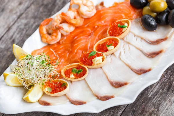 Морепродукты блюдо с ломтиком лосося, пангасиус рыбы, красная икра, креветки, украшенные оливками и лимоном на деревянном фоне крупным планом. Средиземноморские закуски. Вид сверху — стоковое фото