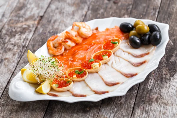 Морепродукты блюдо с ломтиком лосося, пангасиус рыбы, красная икра, креветки, украшенные оливками и лимоном на деревянном фоне крупным планом. Средиземноморские закуски. Вид сверху — стоковое фото