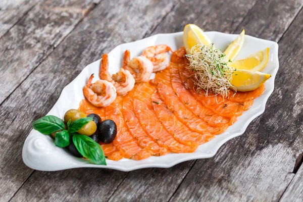 Морепродукты блюдо с ломтиком лосося и креветки, украшенные оливками и лимоном на деревянном фоне крупным планом. Средиземноморские закуски. Вид сверху — стоковое фото