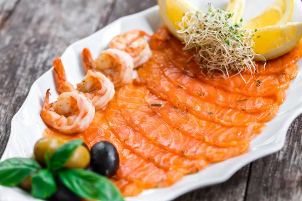 Морепродукты блюдо с ломтиком лосося и креветки, украшенные оливками и лимоном на деревянном фоне крупным планом. Средиземноморские закуски. Вид сверху — стоковое фото