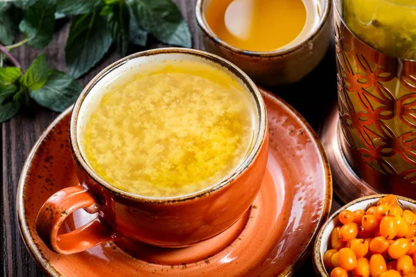 Tee mit Sanddorn in Tasse mit Untertasse, serviert mit Vintage-Teekanne, frischen Beeren, Honig, Minze auf dunklem Holzgrund. gesunde Getränke — Stockfoto