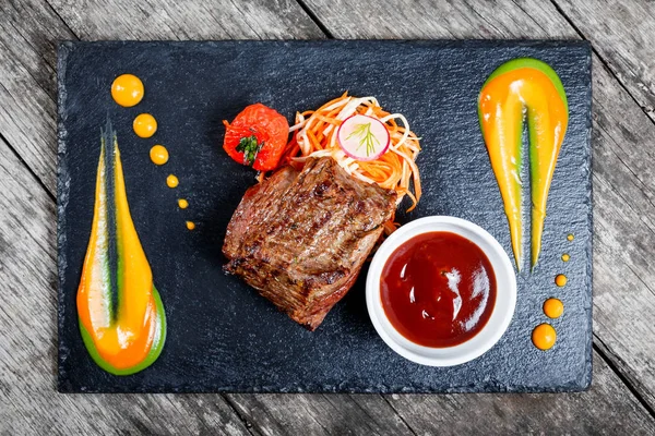 Grilled beef steak with fresh salad and bbq sauce on stone slate background on wooden background close up. Hot Meat Dishes. Top view — Stock Photo, Image