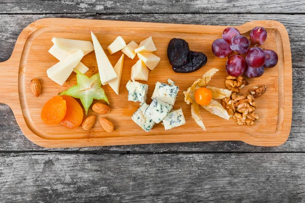 Plateau de fromage garni de poire, miel, noix, raisins, carambole, physalis sur planche à découper sur fond bois. Ensemble de collations et d'apéritifs au vin. Vue du dessus — Photo