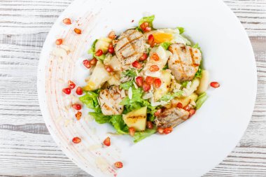 Tavuk göğsü, kavun, ananas, nar taneleri ile taze salata, marul yaprakları ve badem ahşap arka plan üzerinde plaka üzerinde yakın çekim. Üstten Görünüm