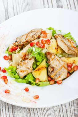 Tavuk göğsü, kavun, ananas, nar taneleri ile taze salata, marul yaprakları ve badem ahşap arka plan üzerinde plaka üzerinde yakın çekim. Üstten Görünüm