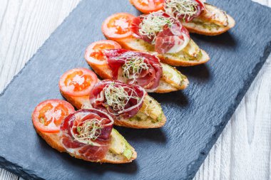 Meze bruschetta salam, domates, kabak ciabatta ekmeği taş arduvaz arka plan üzerinde tarih ile kapatın. Lezzetli aperatifler, sandviçler, crostini, parti ya da piknik zamanında antipasti. Üstten Görünüm